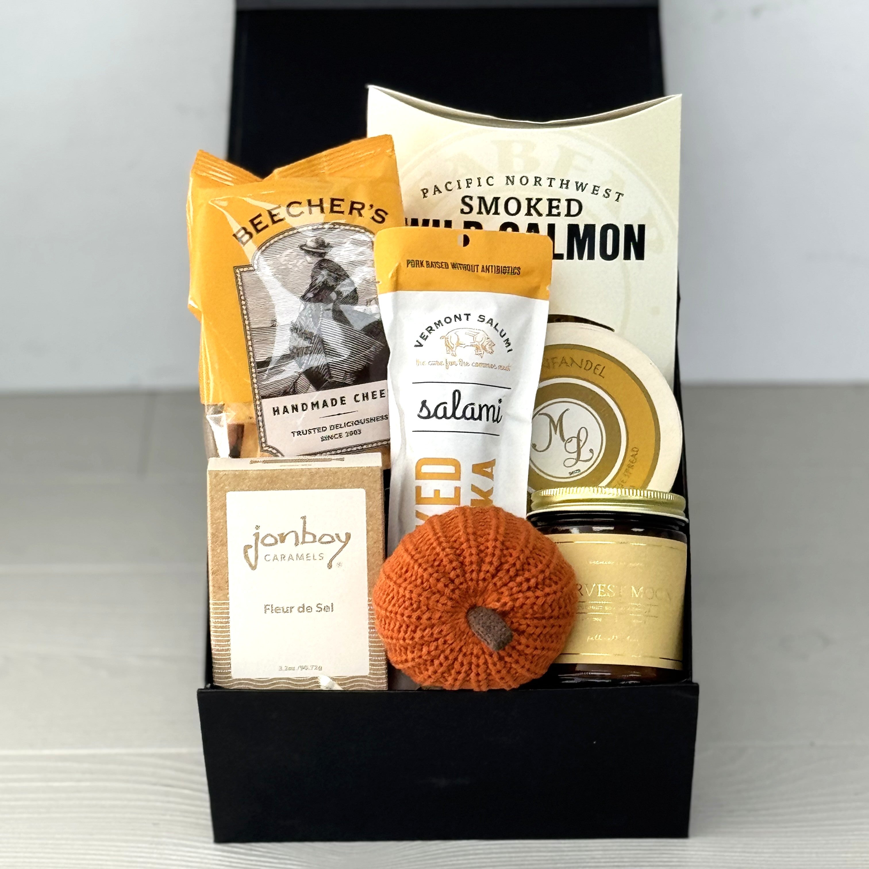 gift basket with crackers, salami, smoked salmon, cheese, scented candle, caramel, packaged in a gift box