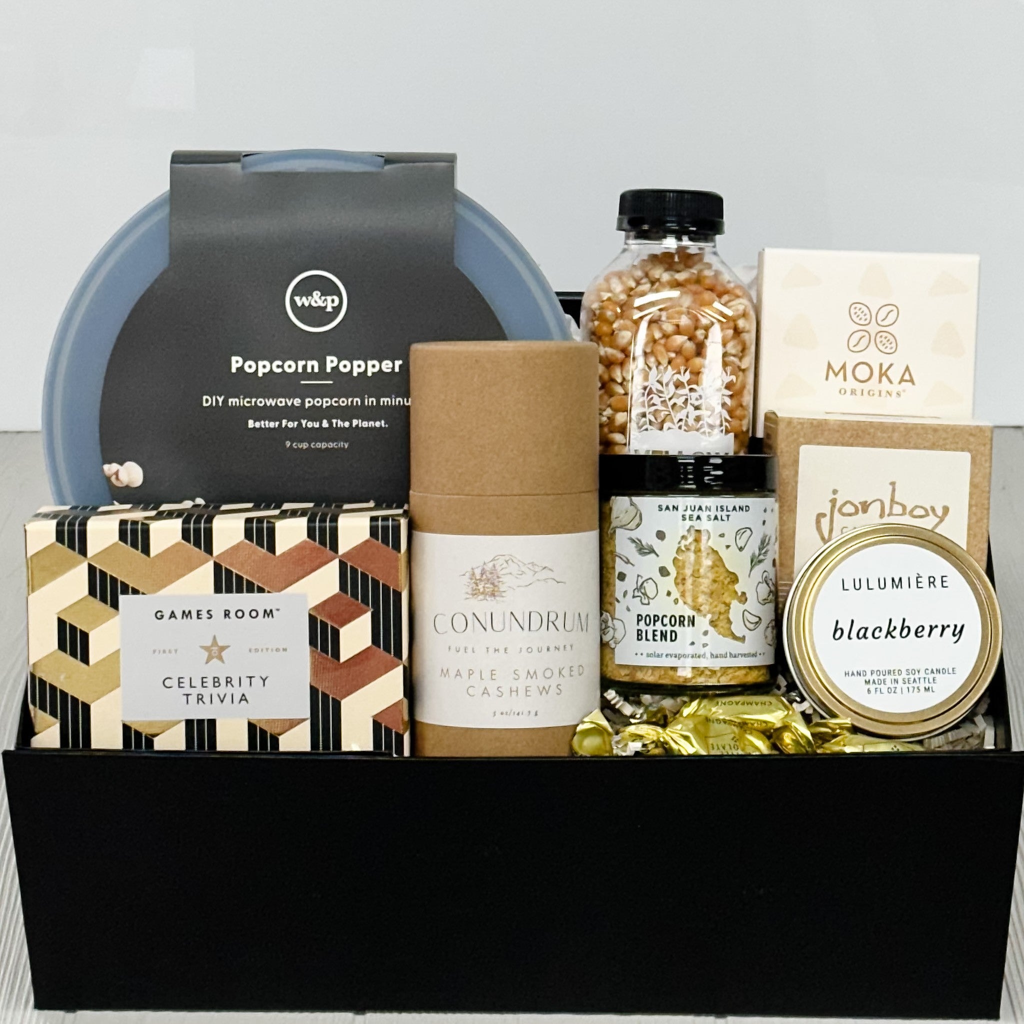 popcorn popping bowl, popcorn, popcorn seasoning salt, celebrity trivia, smoked cashews, chocolate, caramel, scented candle, truffles all part of our game night gift baskert.