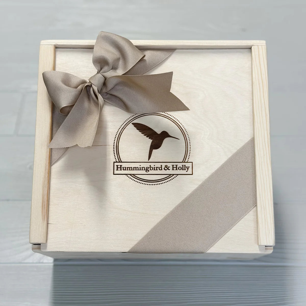 Wooden gift box with a bow and 'Hummingbird & Holly' logo on a gray background.