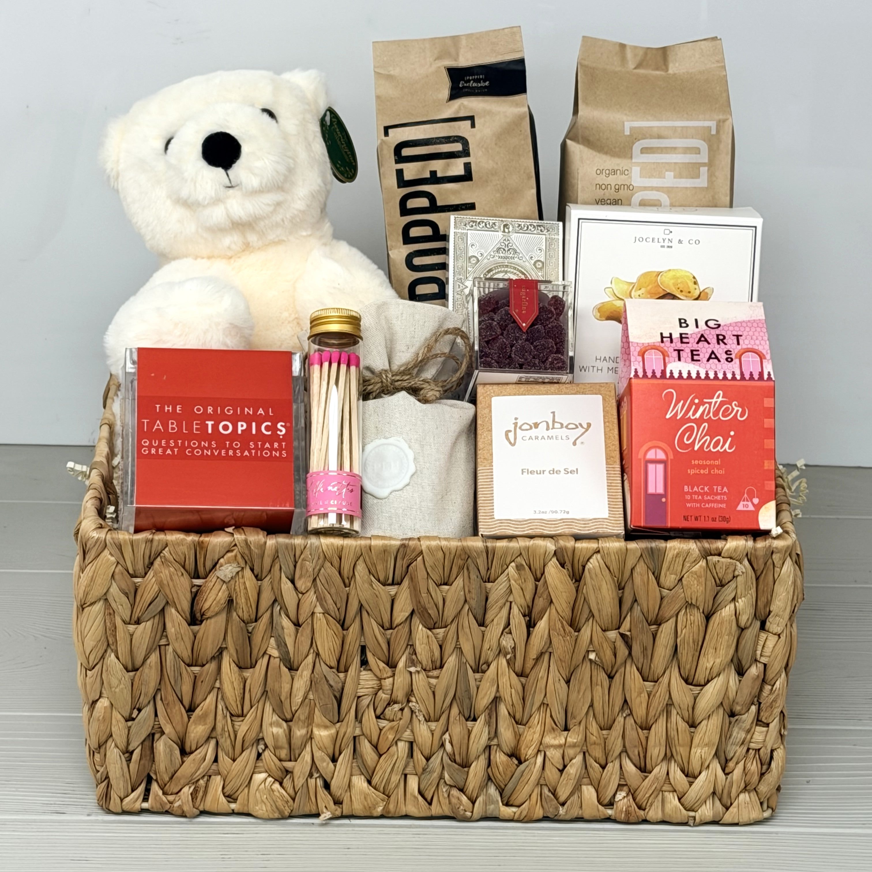 Gift basket with teddy bear, tea packages, and other items on a wooden surface.