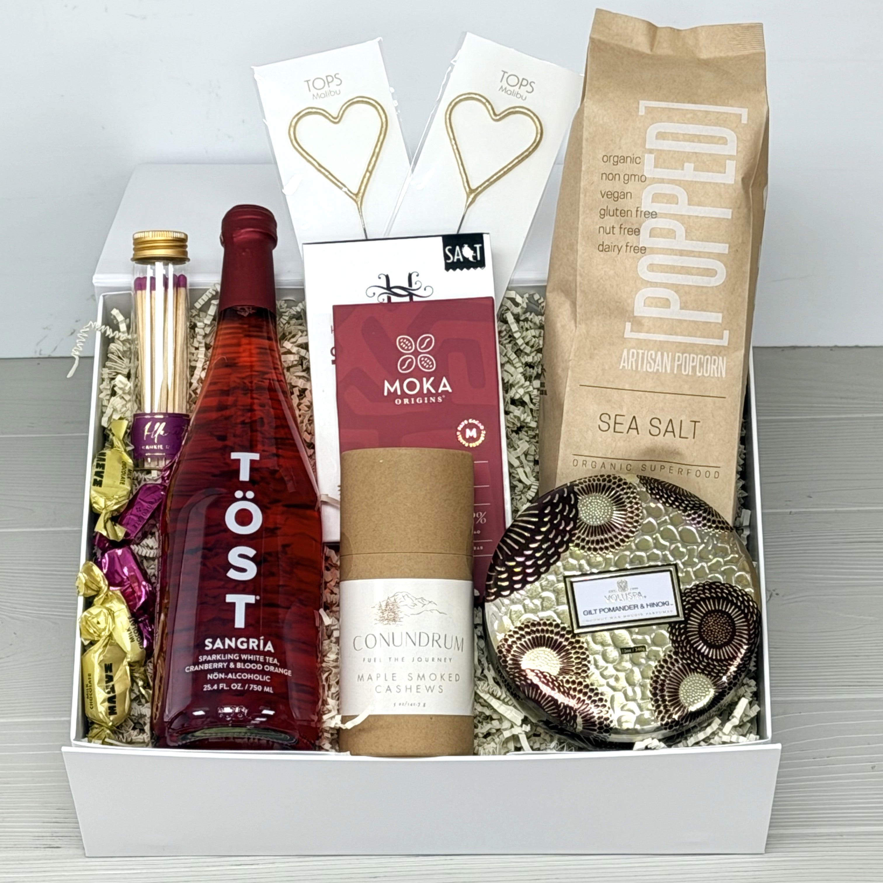 Gift basket with Töst sangria, popcorn, and other items on a white background