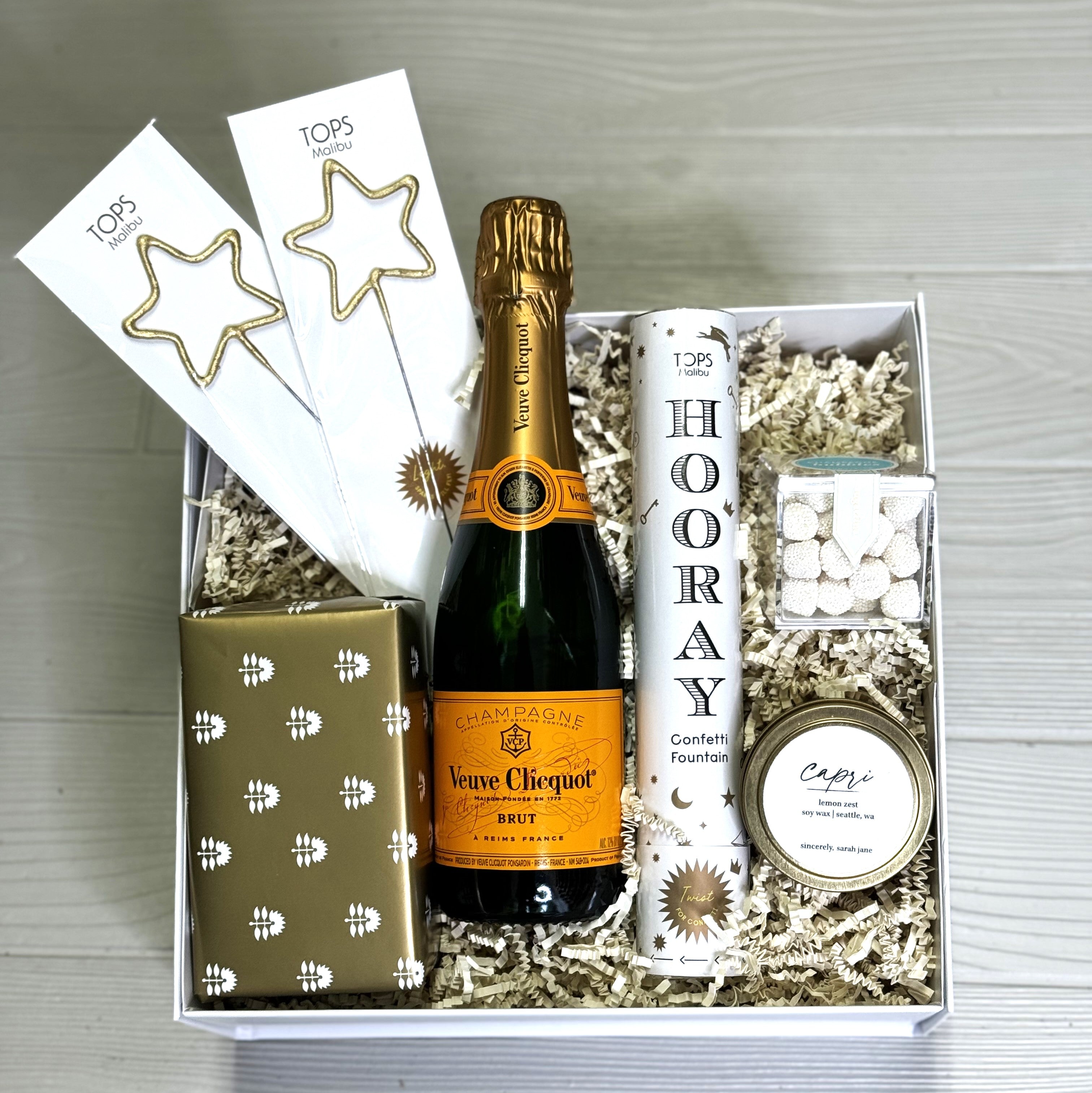 Celebratory gift baskets includes Veuve Champagne, sparklers, cookies, confetti fountain, candle, Sugarfina candy, packaged in a luxury gift box