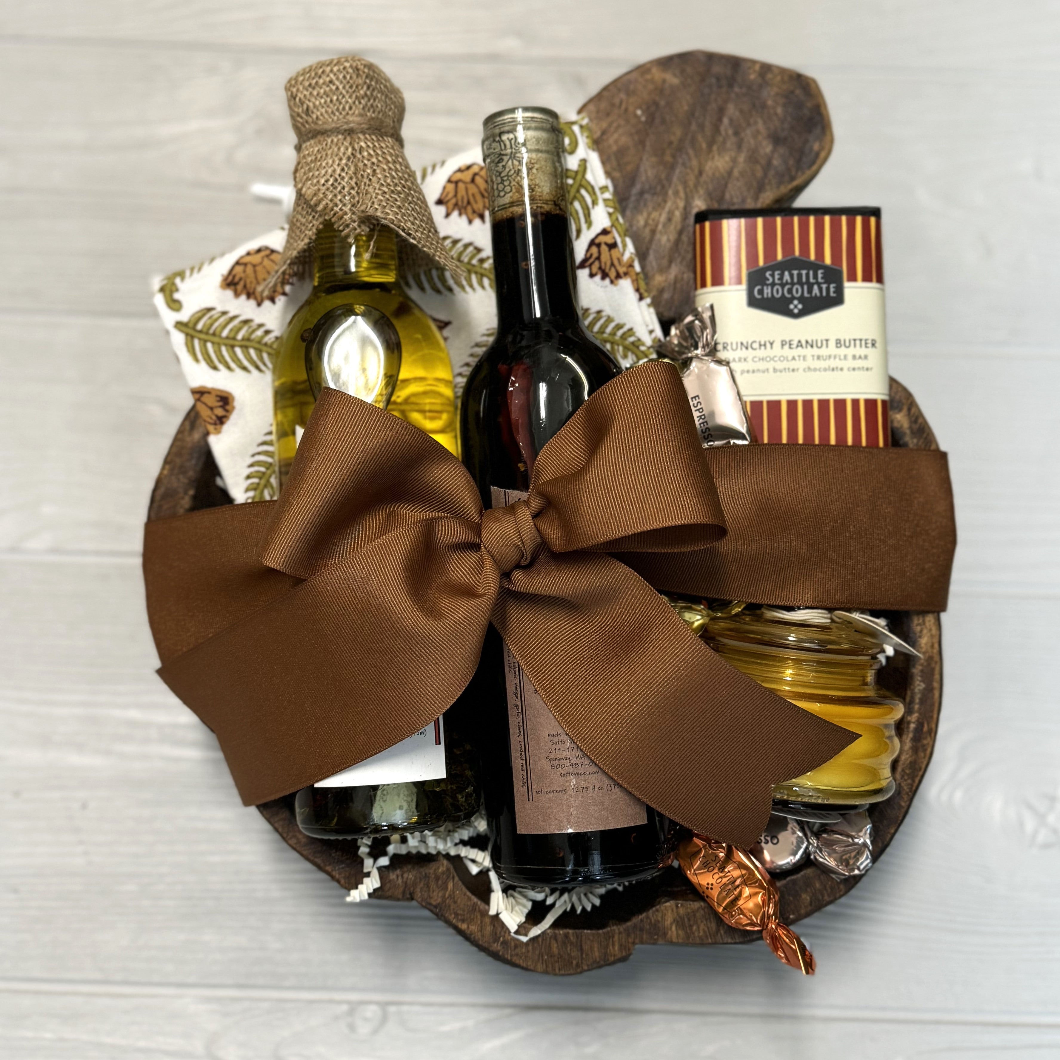 housewarming gift includes olive oil, balsamic vinegar, chocolate, candle, kitchen towel, wooden tray