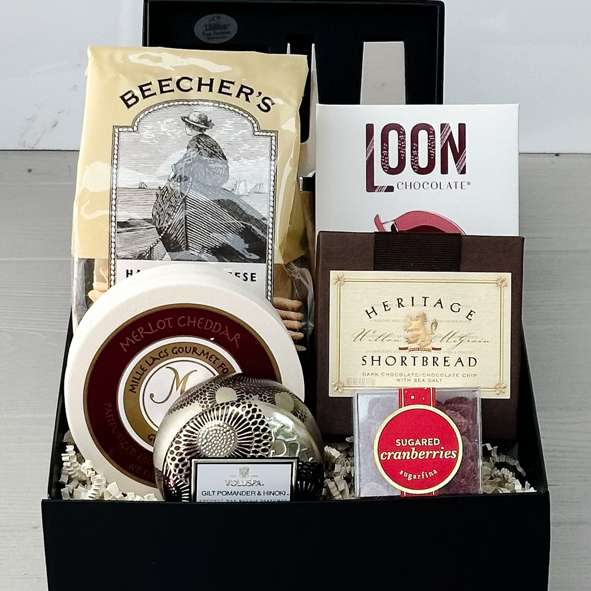 cheese knives, crackers, cheese, shortbread, chocolate, sugared cranberries and a candle all included in our mini holiday charcuterie gift basket.