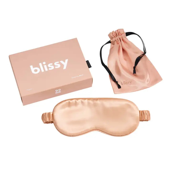 Rose gold sleep mask with packaging and drawstring bag on a white background.