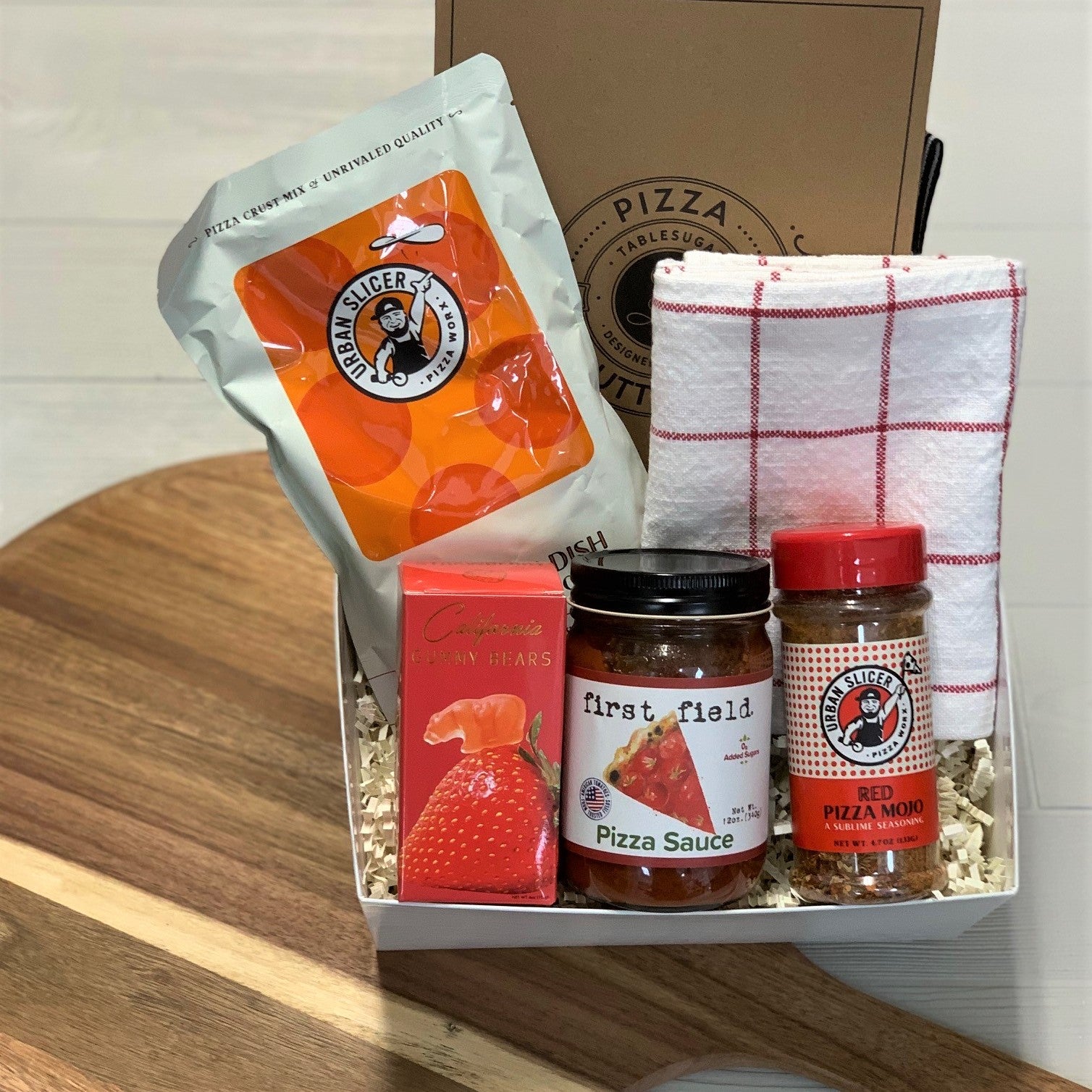 a pizza night gift basket including pizza dough, pizza sauce, pizza spice blend, a kitchen towel, gummy bears, a pizza cutter, and a pizza peel.