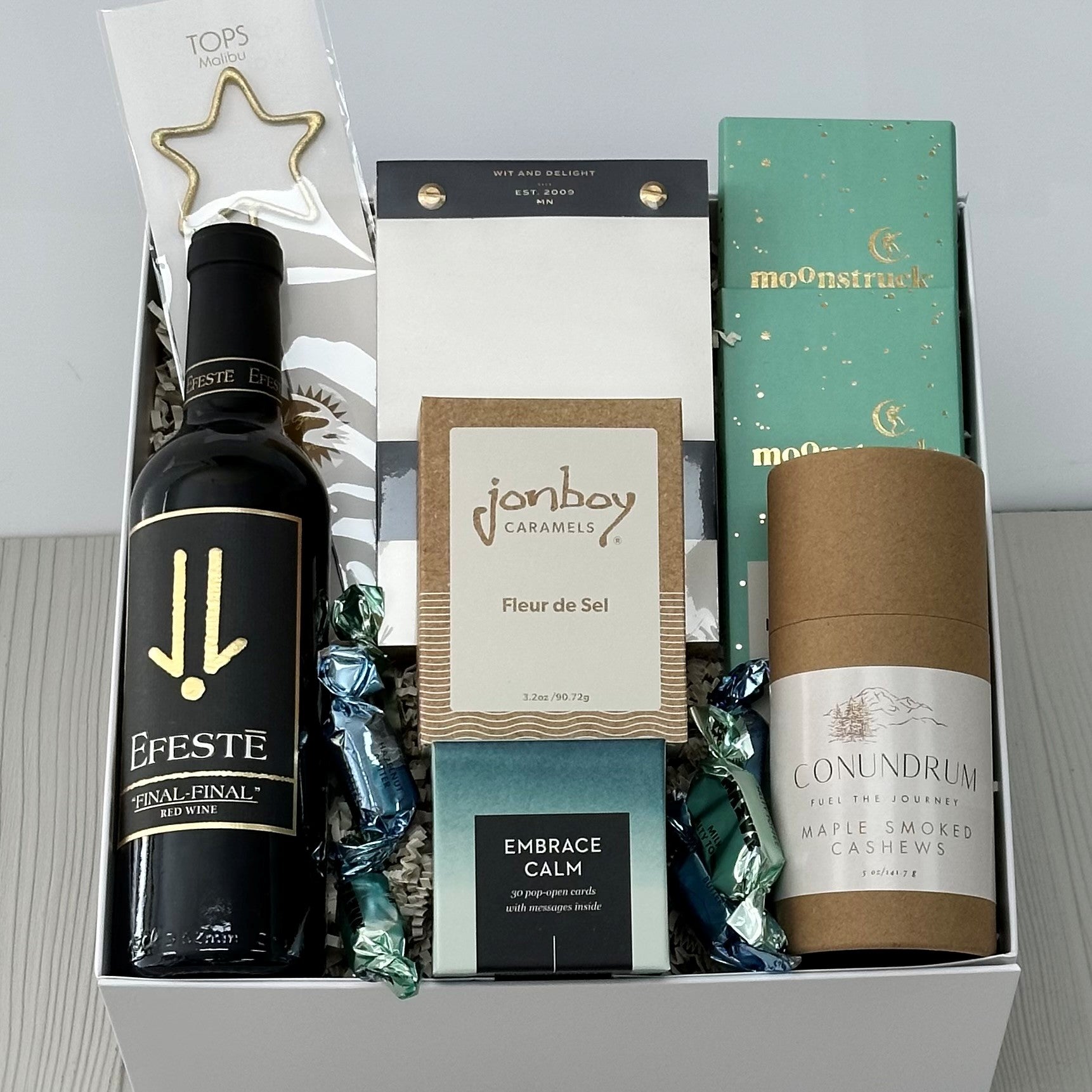 this spring gift basket includes Efeste Final Final red wine, a star-shaped sparkler by Tops malibu, notepad, caramel, chocolate, cashews, boxed quotes 