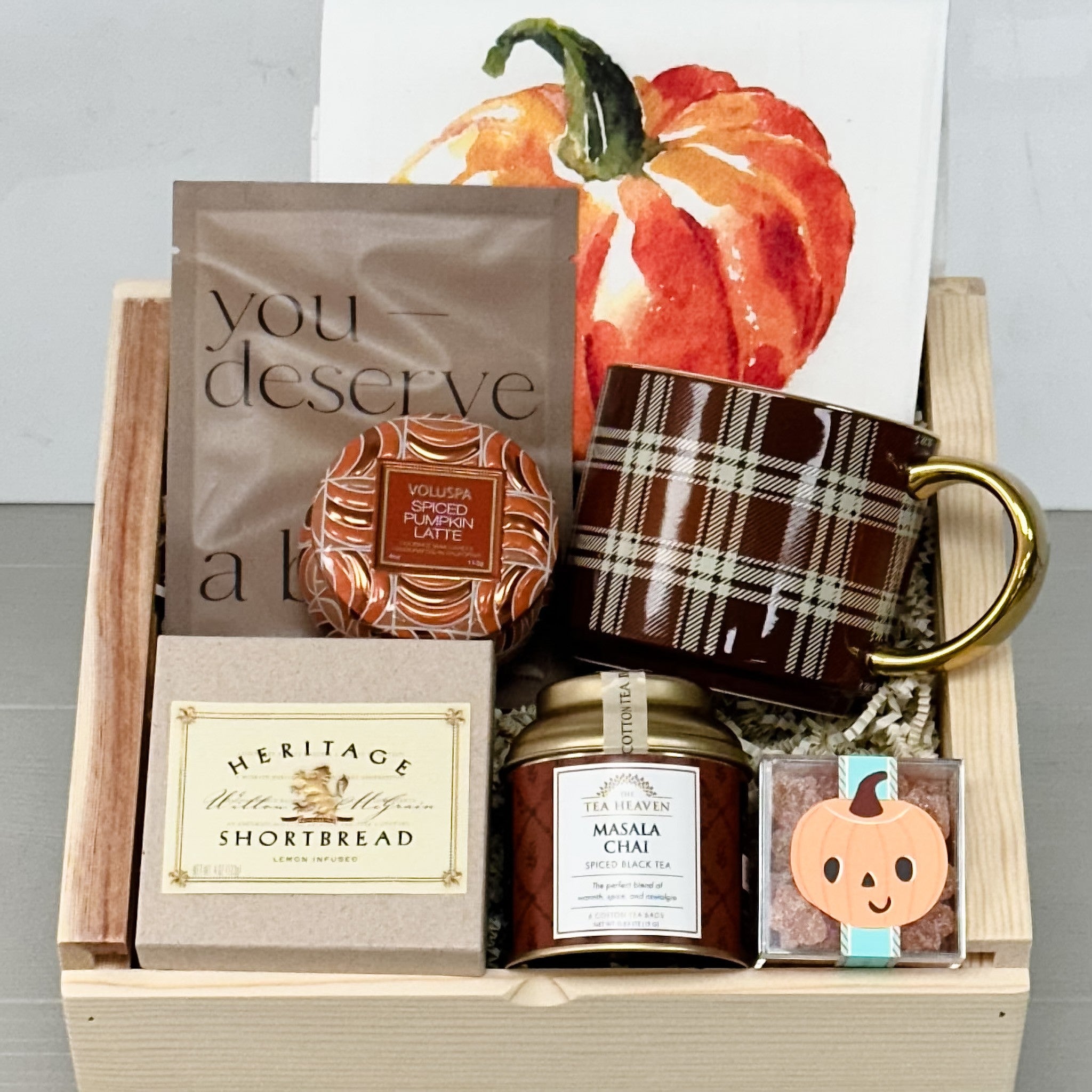 Gift basket with pumpkin spice latte, mug, shortbread, and candles on a light background
