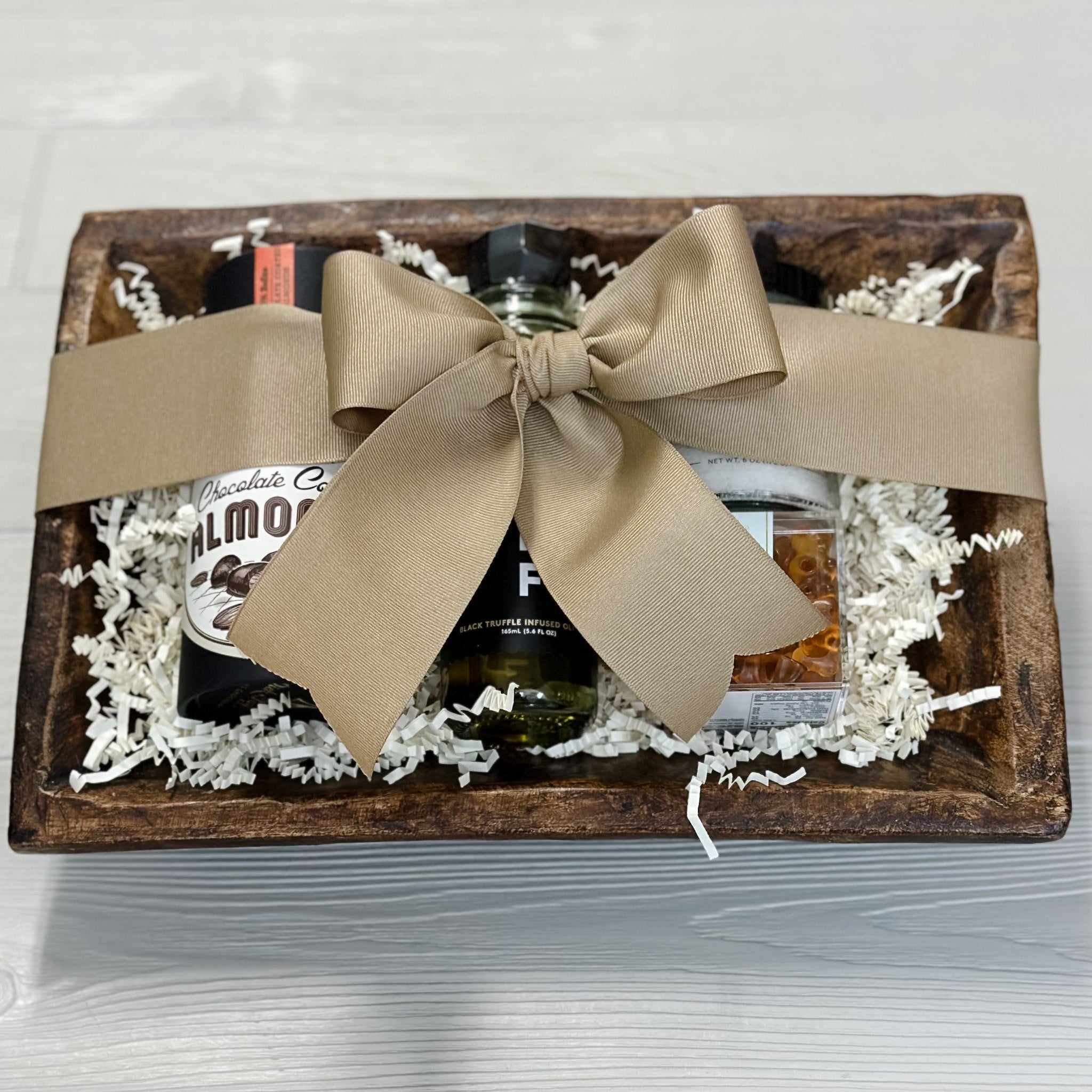 top view of housewarming gift basket with chocolate covered almonds, truffle oil, sea salt, sugarfina gummies in wooden dough bowl