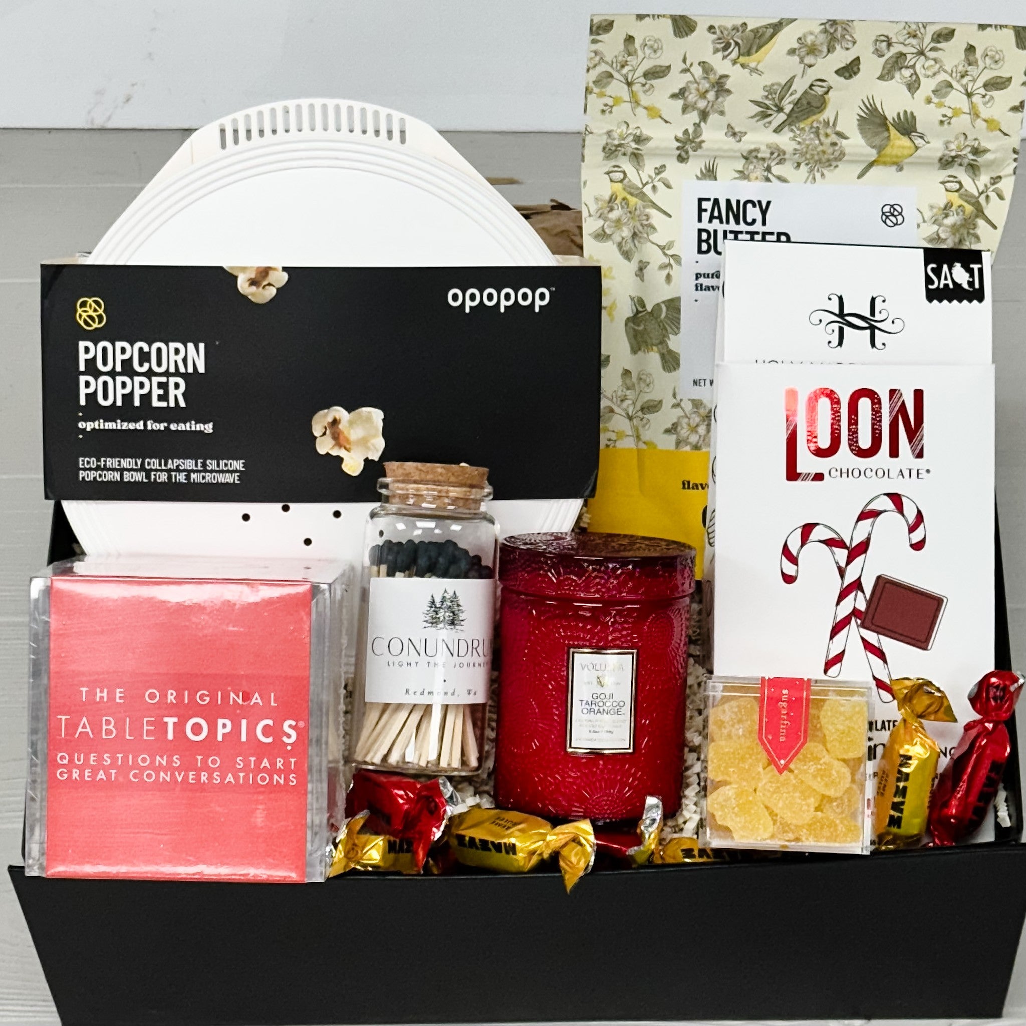 popcorn popper, popcorn, chocolate toffee, sugarfina, candle, matched, tabletopics, truffles all packaged in our family fun night gift basket.