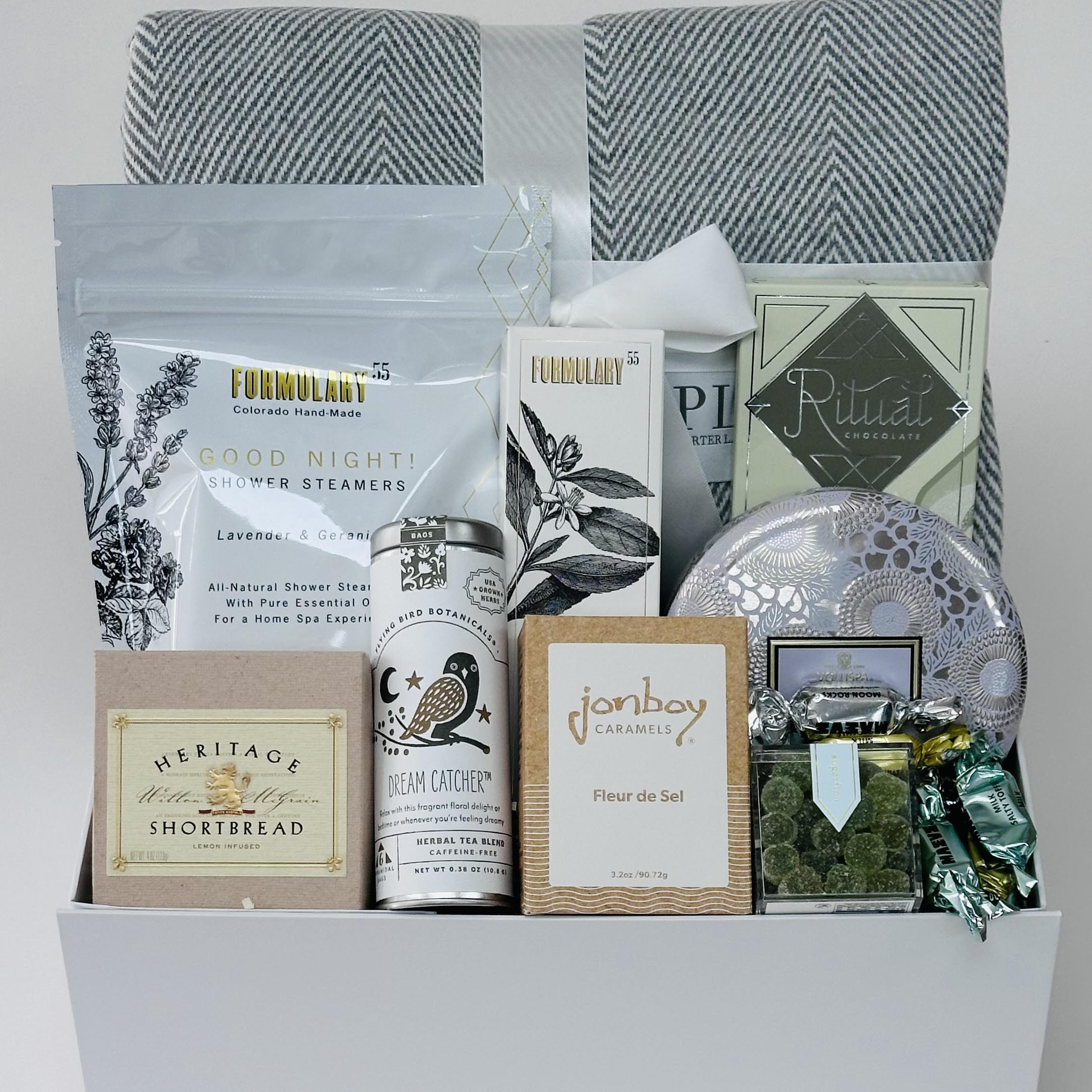 Herringbone blanket, shower steamers, hand cream, chocolate, candle, candy, caramel, tea, shortbread, all included in a gift box.