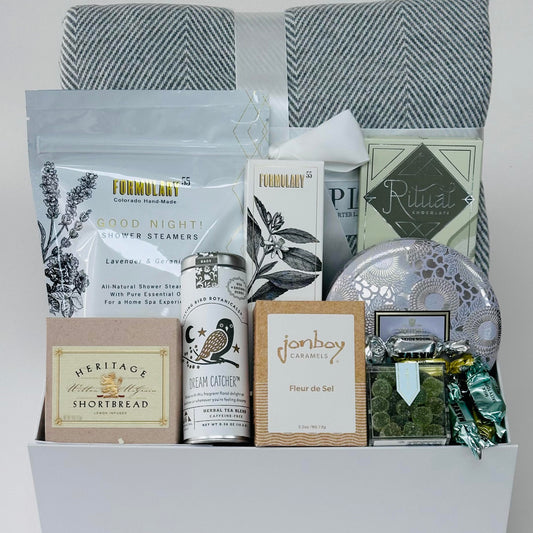Herringbone blanket, shower steamers, hand cream, chocolate, candle, candy, caramel, tea, shortbread, all included in a gift box.