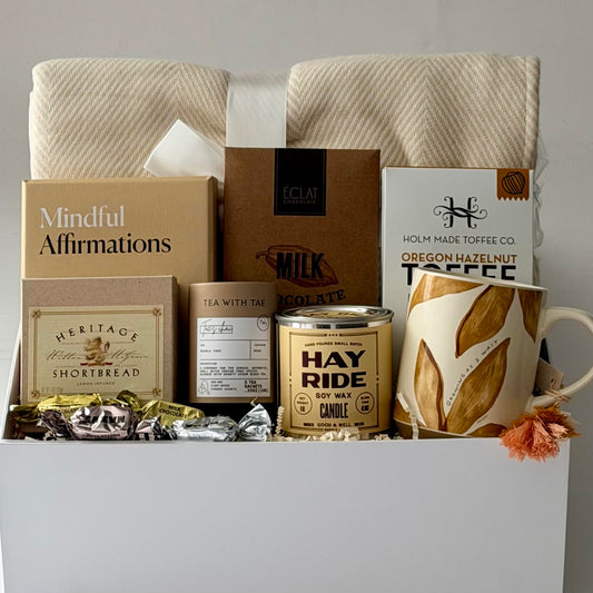 Gift box with cozy blanket, mug, tea, chocolate, mindfulness cards, toffee, candle, shortbread.