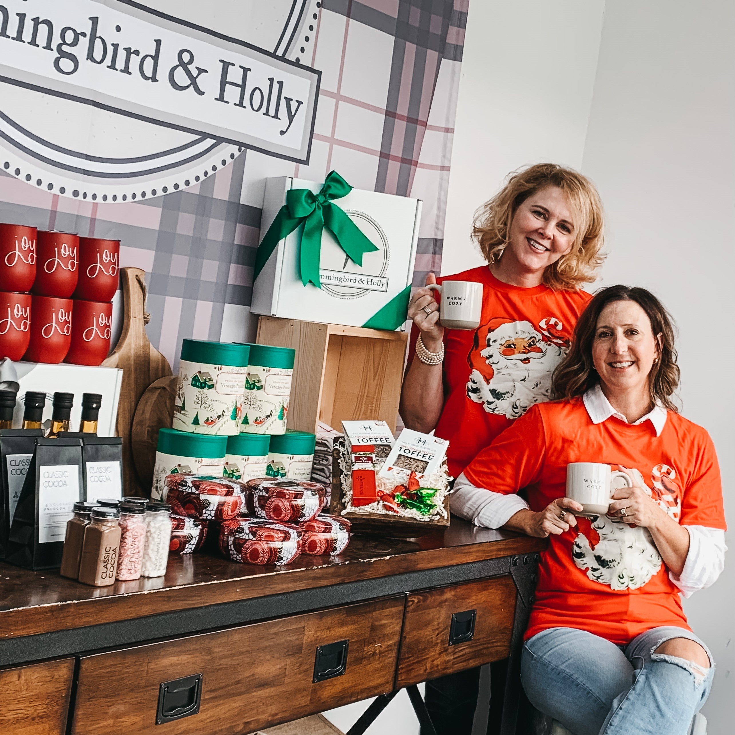 Kate and Krista, Hummingbird and Holly owners, in front of holiday gift baskets