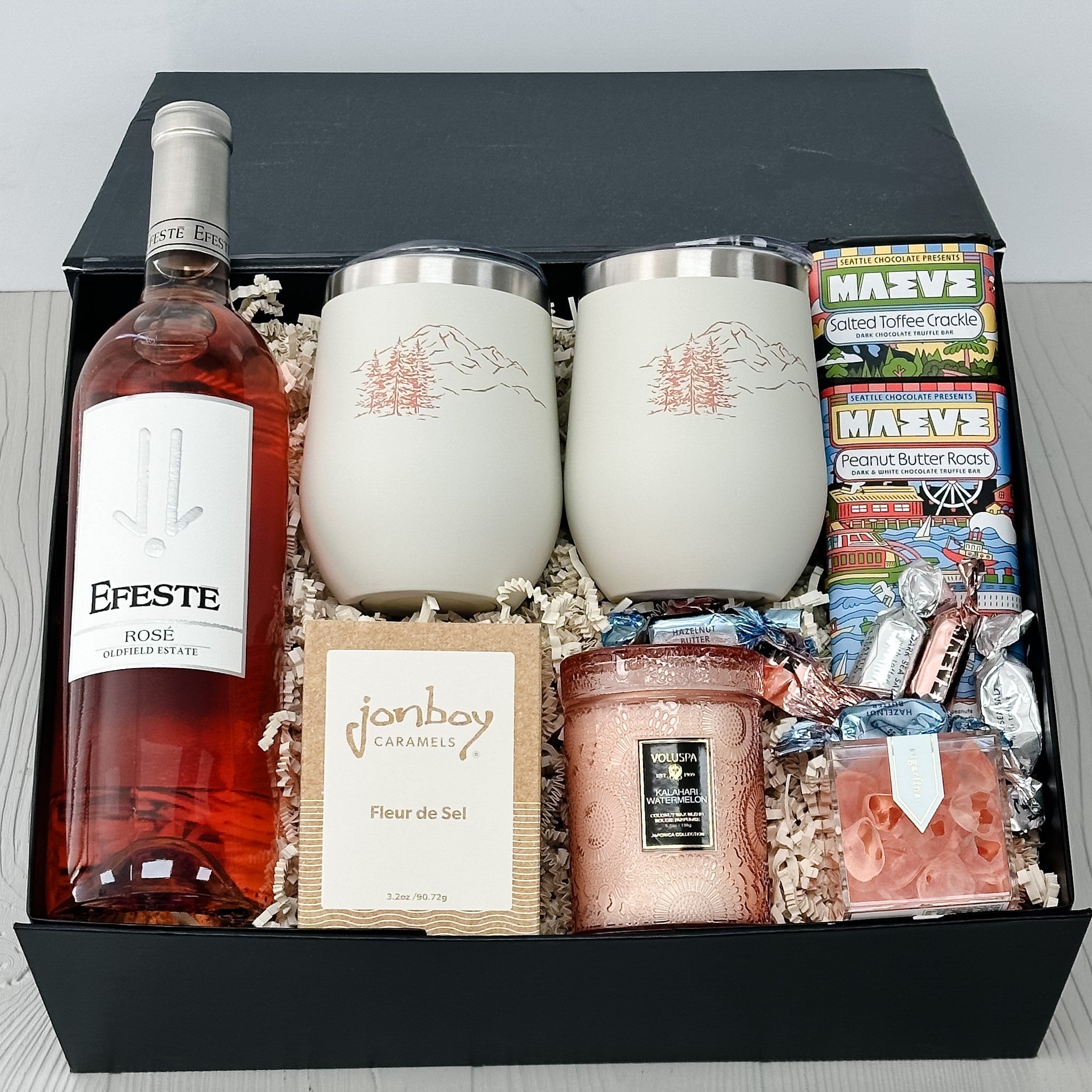 bottle of rose, chocolate, wine tumblers, caramel, candle, candy, truffles all included in our pnw springtime happy hour gift basket.