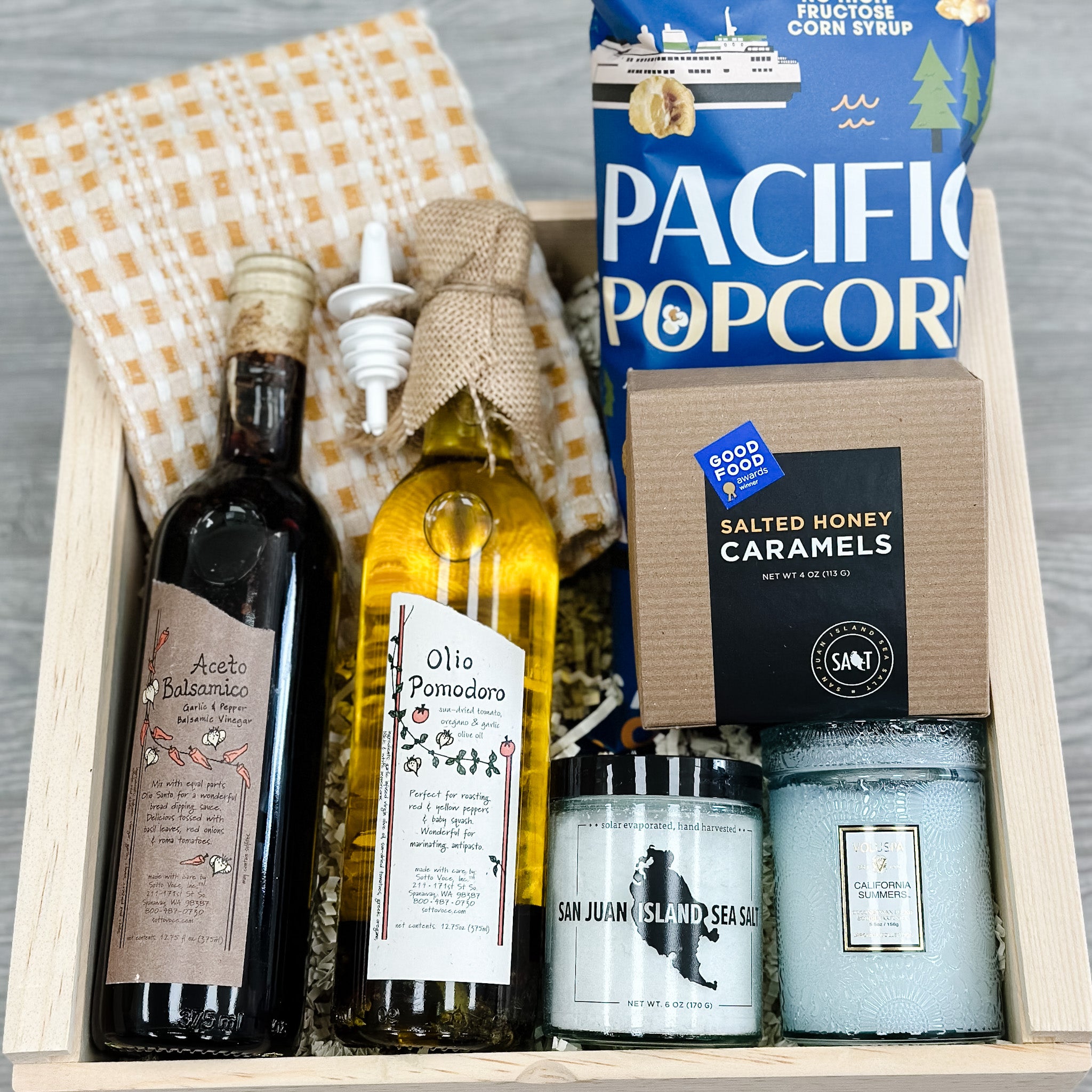 dish towel, olive oil, balsamic vinegar, caramel cheddar popcorn, caramel, sea salt, scented candle all included in our pnw summer housewarming gift box.