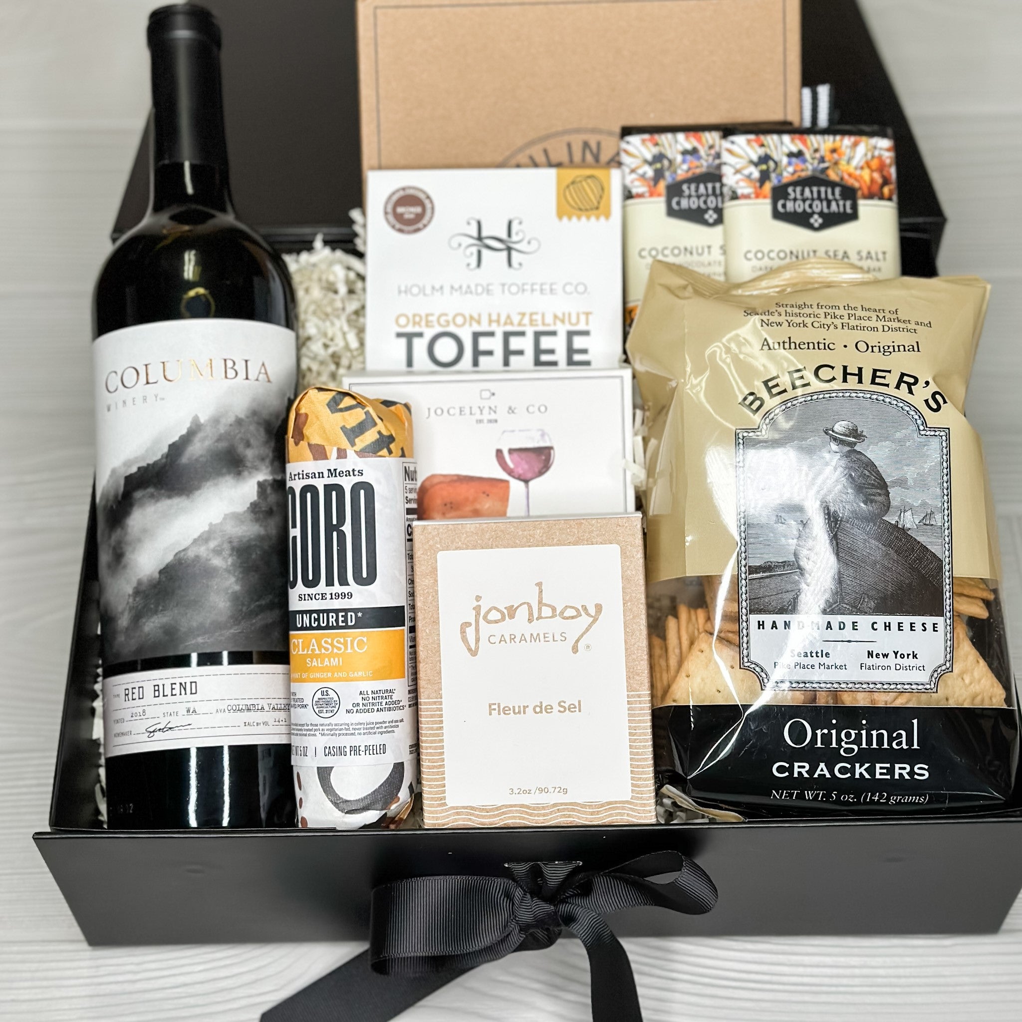 Charcuterie gift that includes red wine, salami, caramel, cheese, toffee, cheese knives, chocolate, and crackers.