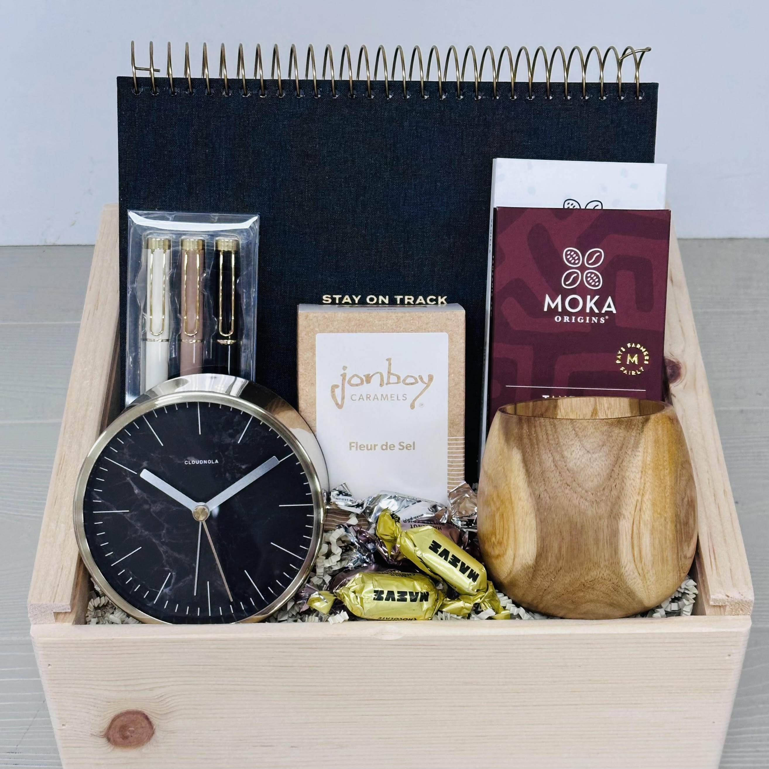 Gift basket with a desktop calendar, desktop clock, motivational pens, chocolate, caramel, bonbons, and a scented candle.  