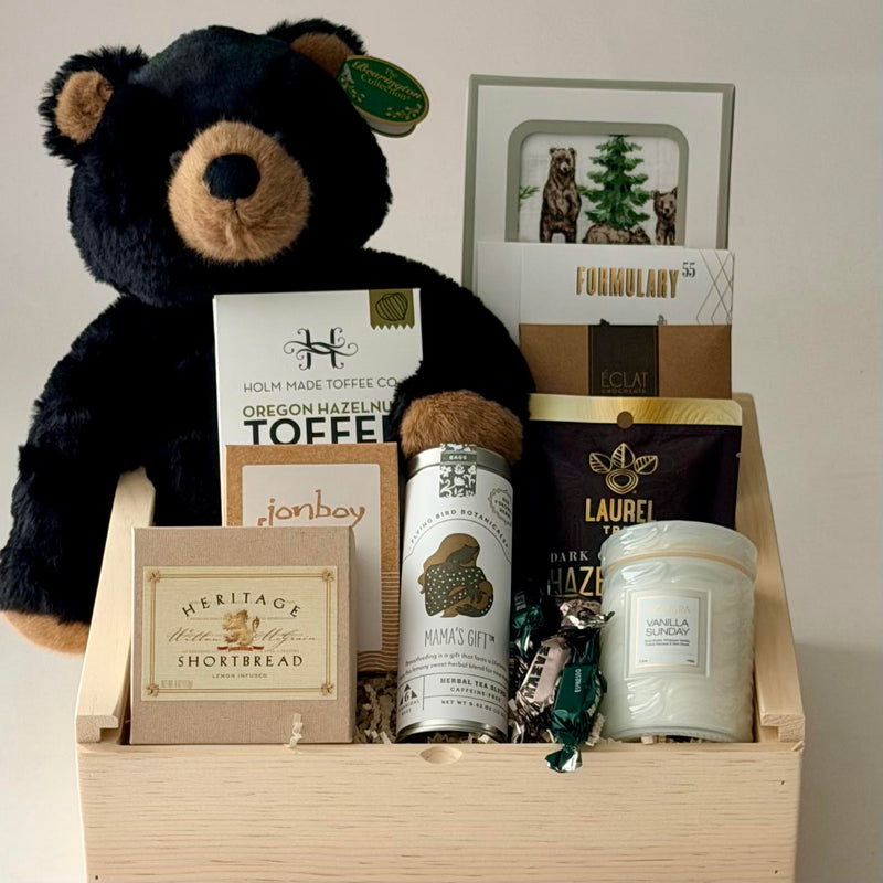 Wooden gift box with stuffed teddy bear, bear and evergreen tree swaddle blanket, face mask, chocolate, toffee, hazelnuts, candle, tea, caramel, shortbread, bonbons.