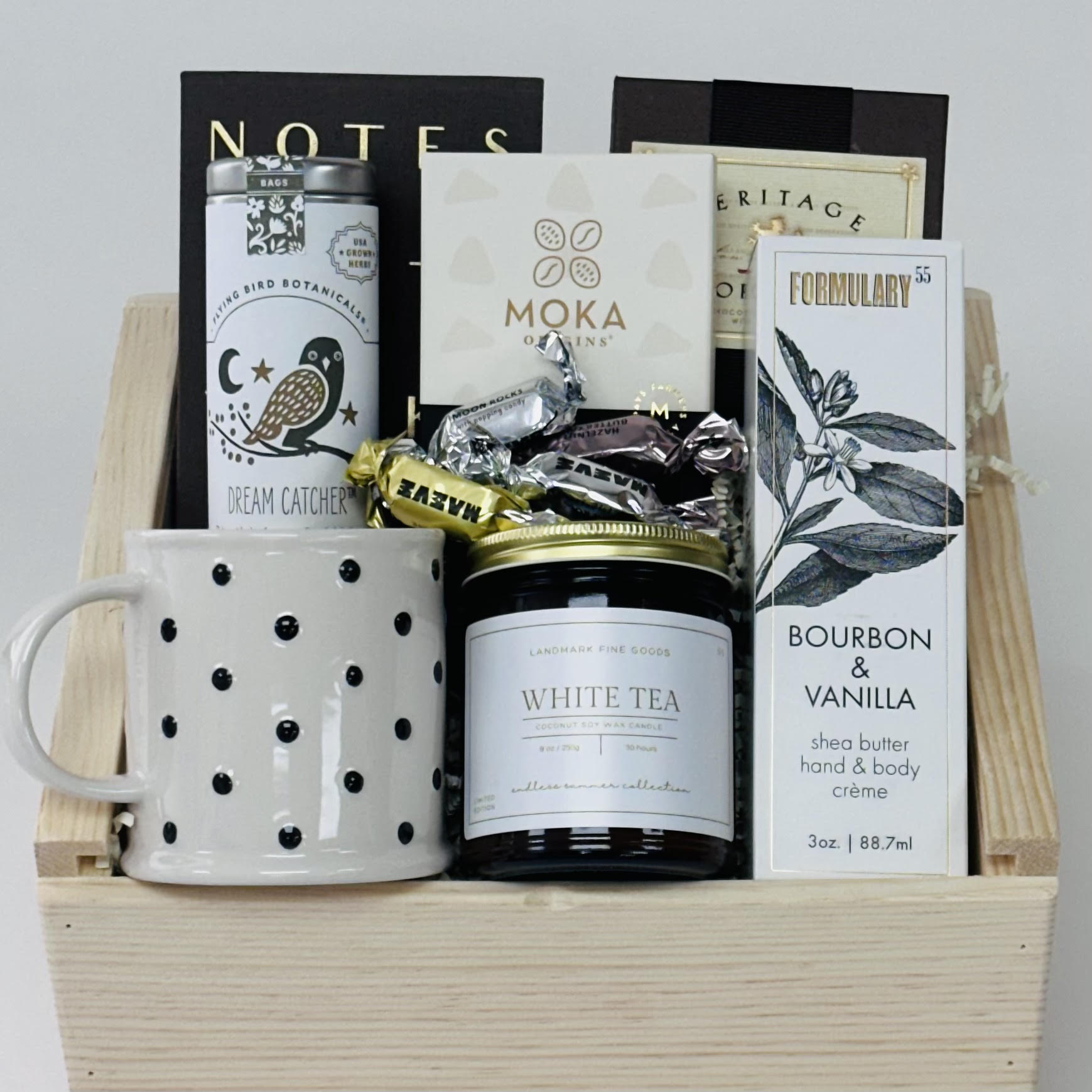 polka dot mug, tea, shortbread, notebook, chocolate, candle, and hand lotion in a wooden slide lid box included in our comfort edit gift box. 