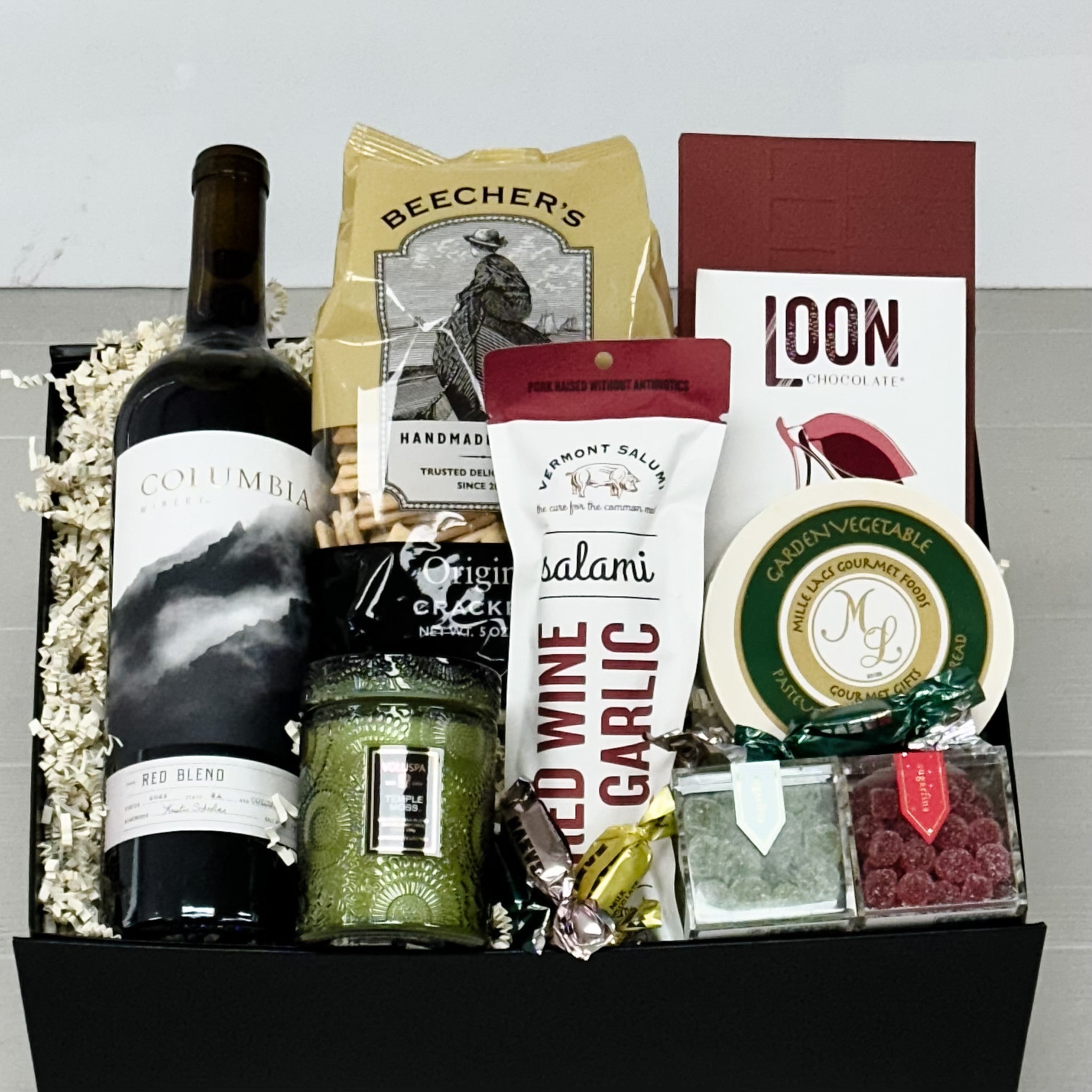 Gift basket with wine, salami, and other snacks on a white background