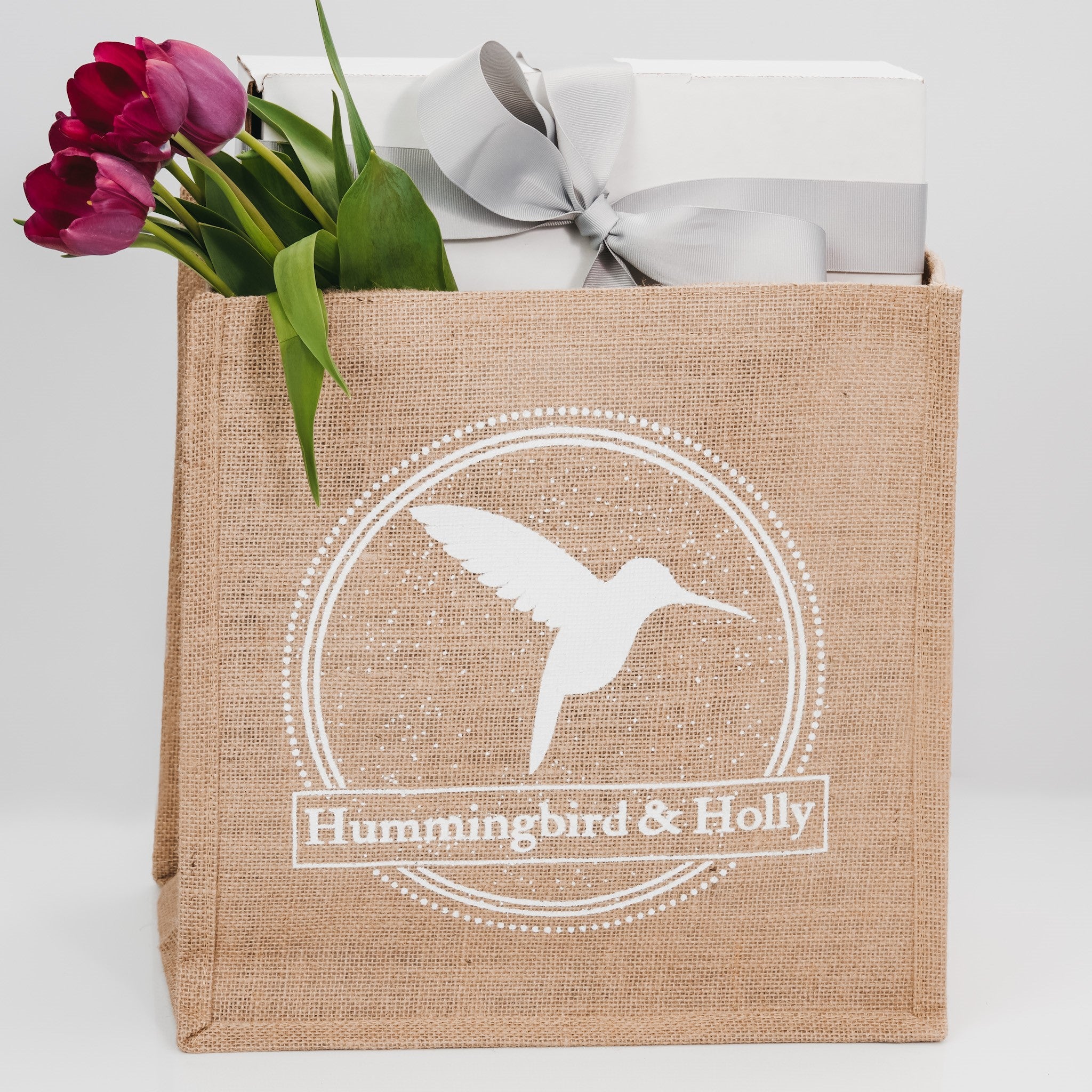 Closeup of natural jute tote with Hummingbird and Holly logo.